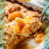 A close-up of a peach dump cake served in a baking dish, featuring a golden crumb topping and juicy peach filling, with a spoon lifting a portion.
