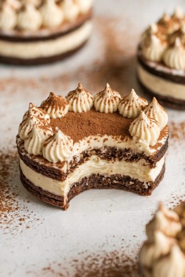 A tiramisu sandwich cookie with elegant cocoa powder dusting on top, showcasing multiple layers of chocolate cookie and mascarpone filling. The text overlay "Tiramisu Sandwich Cookies" enhances the appeal for dessert lovers looking for a refined, Italian-inspired treat.