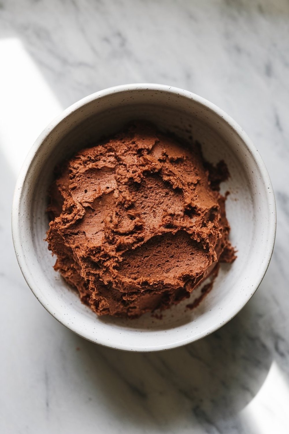 A bowl of thick, chocolate cookie dough with a smooth, fudgy texture. The deep brown color hints at its intense chocolate flavor, ideal for creating the cookie layers in tiramisu sandwich cookies.