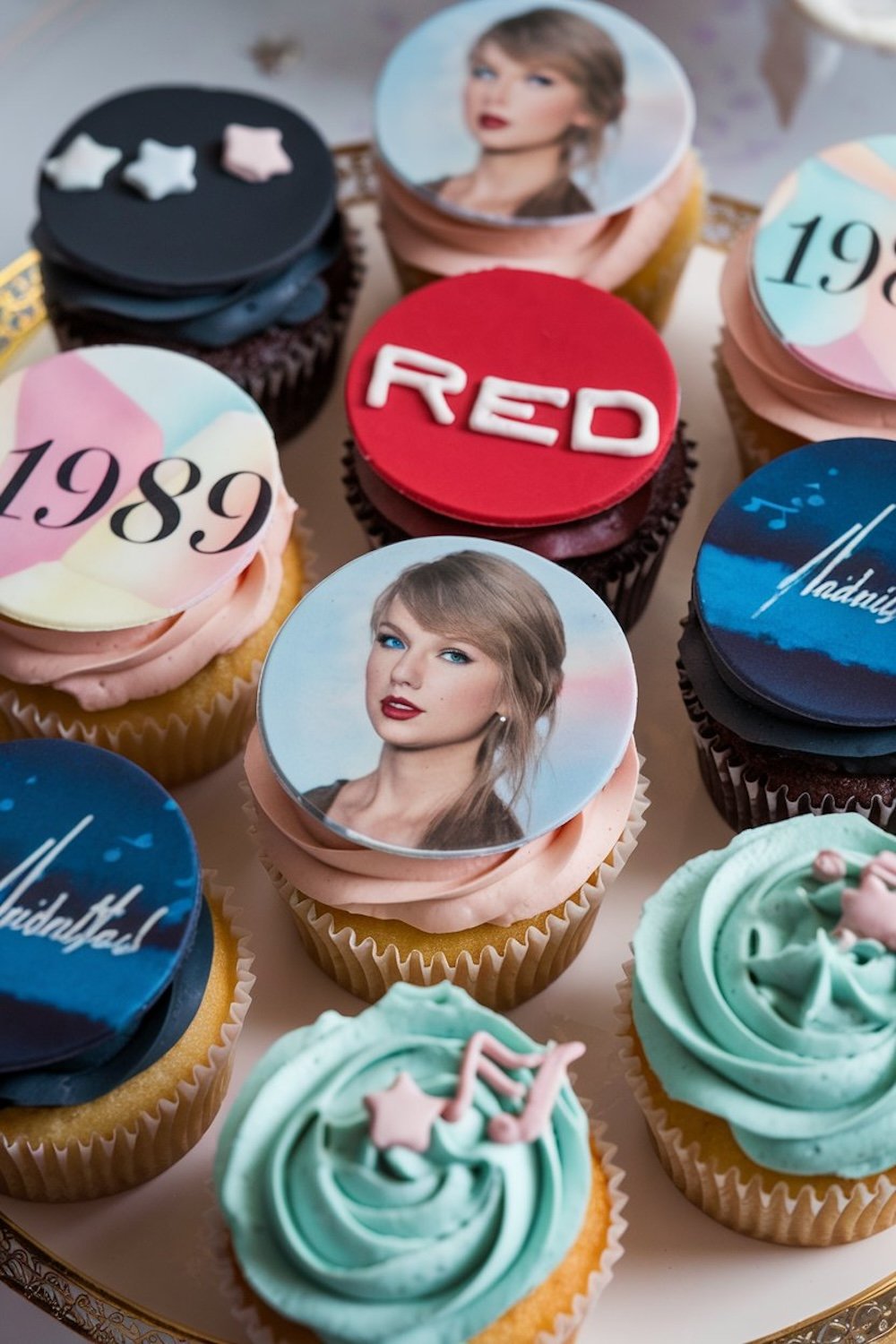 A variety of cupcakes decorated with themes from Taylor Swift’s albums, including "Red," "1989," and a fondant image of Taylor Swift.