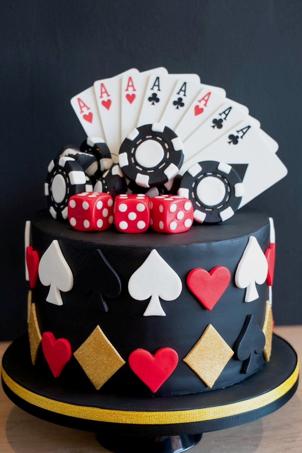 A lavish multi-layered cake in red and black with diamond patterns and a cascade of poker chips.