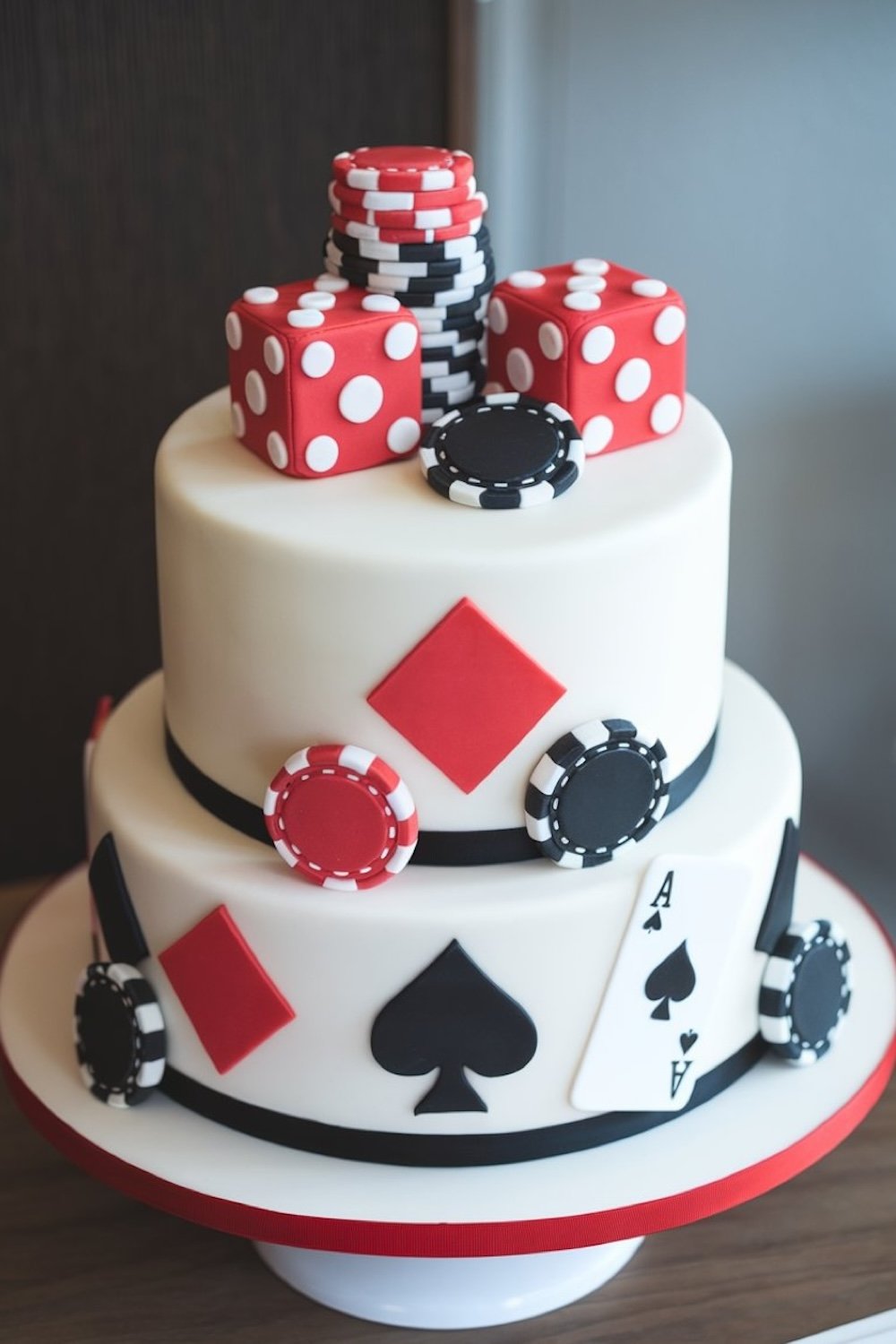 A sleek round cake decorated with red and black card suits and poker chips, echoing a professional poker table.