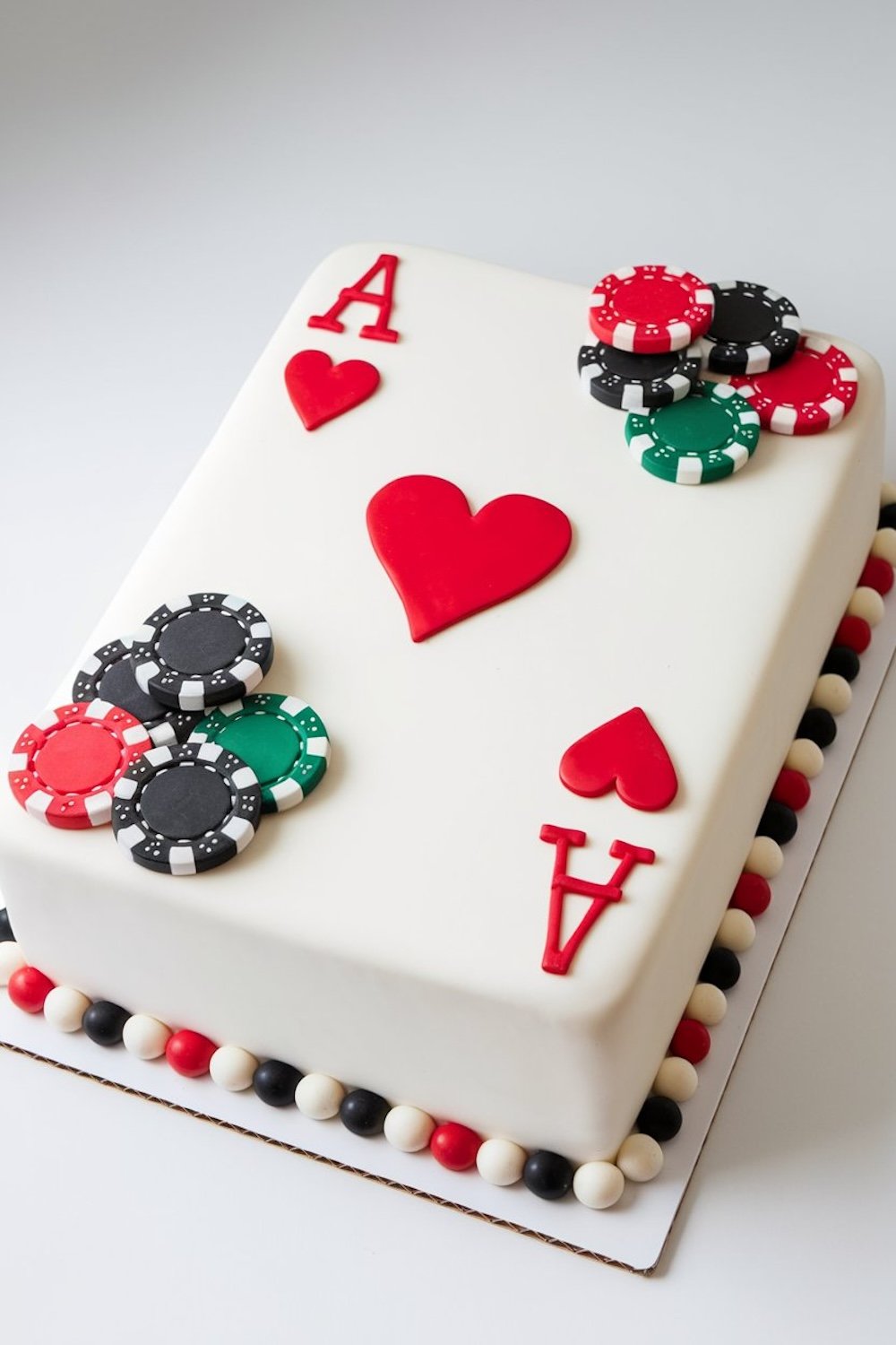 An opulent black tiered cake adorned with poker chip accents and red highlights, perfect for a casino-themed celebration.