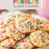 Brightly colored Fruity Pebbles Sugar Cookies piled on a plate, with a playful, multi-colored text label above, set against a soft, domestic background.