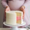 Pregnant woman holding a gender reveal cake with a slice cut to show pink filling, revealing the baby's gender.