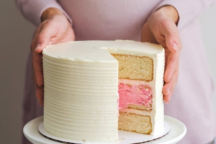 Pregnant woman holding a gender reveal cake with a slice cut to show pink filling, revealing the baby's gender.