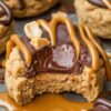A peanut butter cookie cut in half to reveal a soft chocolate filling, artistically drizzled with caramel on a caramel-smeared surface.