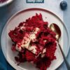 A delicious serving of red velvet dump cake topped with whipped cream, ready to be enjoyed on a white plate with a spoon.