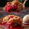 A spoonful of rhubarb dump cake with vibrant red rhubarb filling dripping over a dark wooden table, accompanied by a scoop of vanilla ice cream, with text overlay 'simple RHUBARB DUMP CAKE with cake mix'.