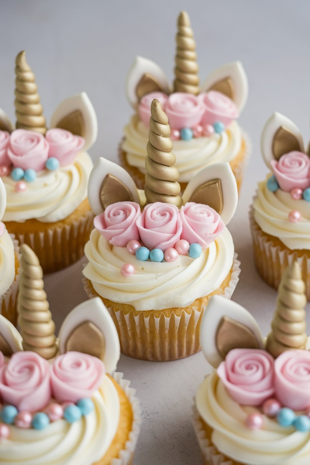 Unicorn cupcakes with golden horns, pink fondant roses, and pastel pearls, arranged on a light background for an elegant presentation.