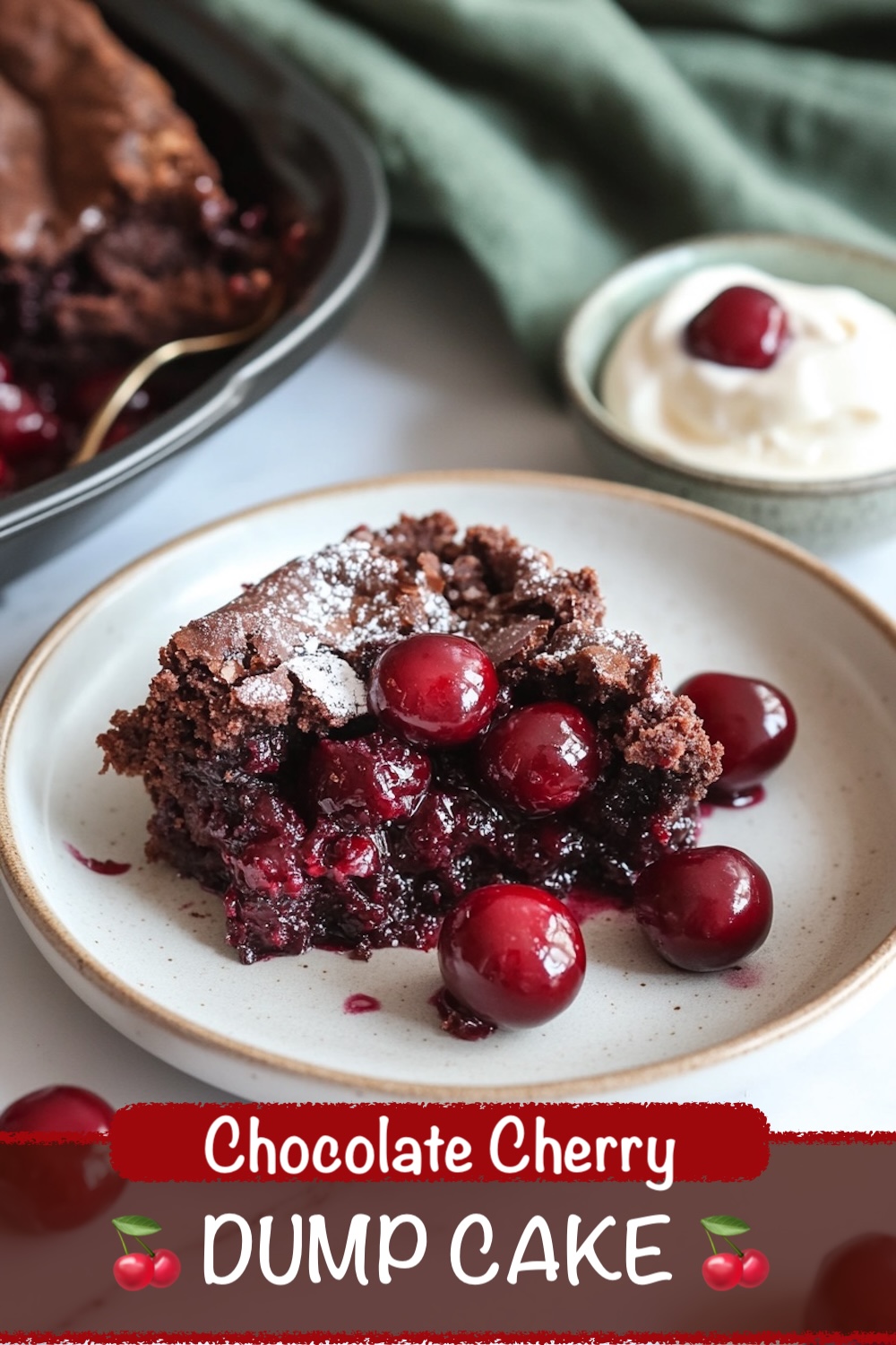 A close-up of a chocolate cherry dump cake slice on a plate. The moist, chocolatey cake is bursting with whole cherries and garnished with powdered sugar. A side of whipped cream is in the background, and a baking dish filled with the cake sits just beyond. The image is captioned "Chocolate Cherry Dump Cake."
