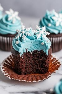 Winter Wonderland Chocolate Cupcakes – 24 Days of Christmas Desserts: Chocolate cupcakes with blue buttercream frosting, topped with intricate white snowflake decorations and pearl sprinkles, featured in "24 Days of Christmas Desserts." These wintry cupcakes evoke a snowy wonderland, making them an enchanting addition to your holiday dessert spread.