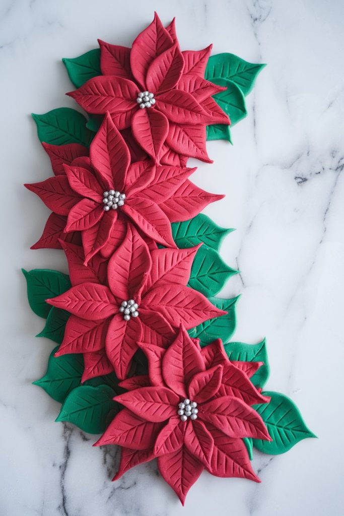 A closer look at the intricate fondant poinsettias, showcasing the fine detailing of the leaves and petals, with silver pearl centers, placed on a marble surface for a festive finish.