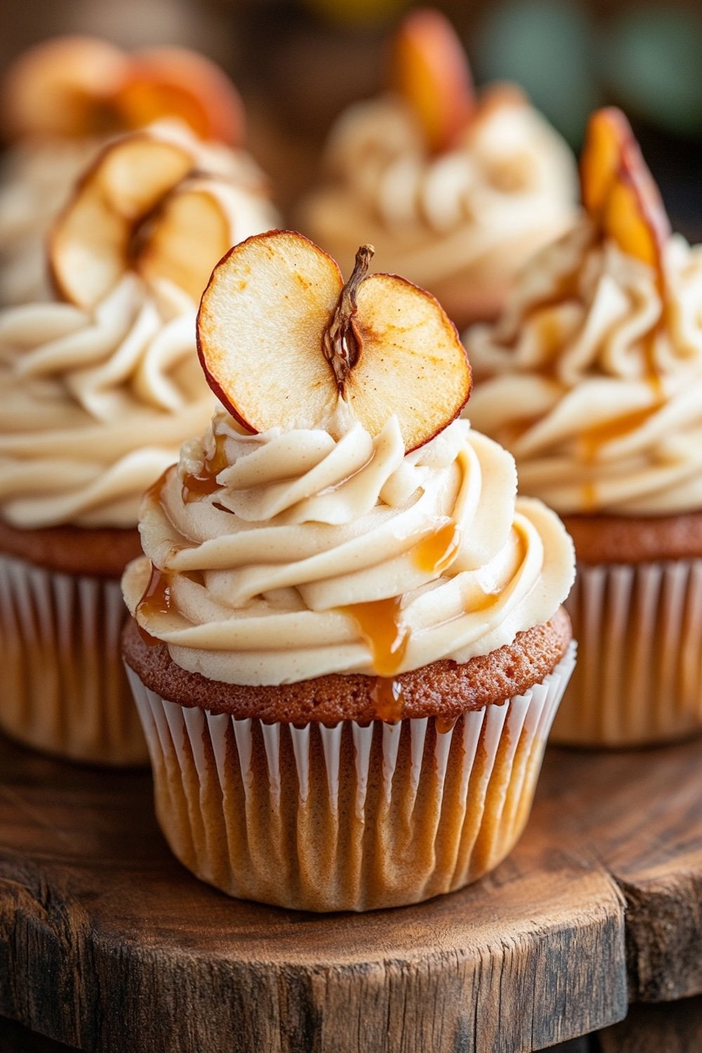 Apple-spiced cupcakes with salted caramel buttercream frosting, drizzled with caramel and a sprinkle of sea salt, displayed on a wooden table with apples and cinnamon.
