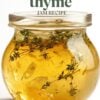 Close-up of a glass jar filled with apple thyme jam, garnished with fresh thyme sprigs, highlighted by a text overlay 'homemade apple thyme jam recipe'