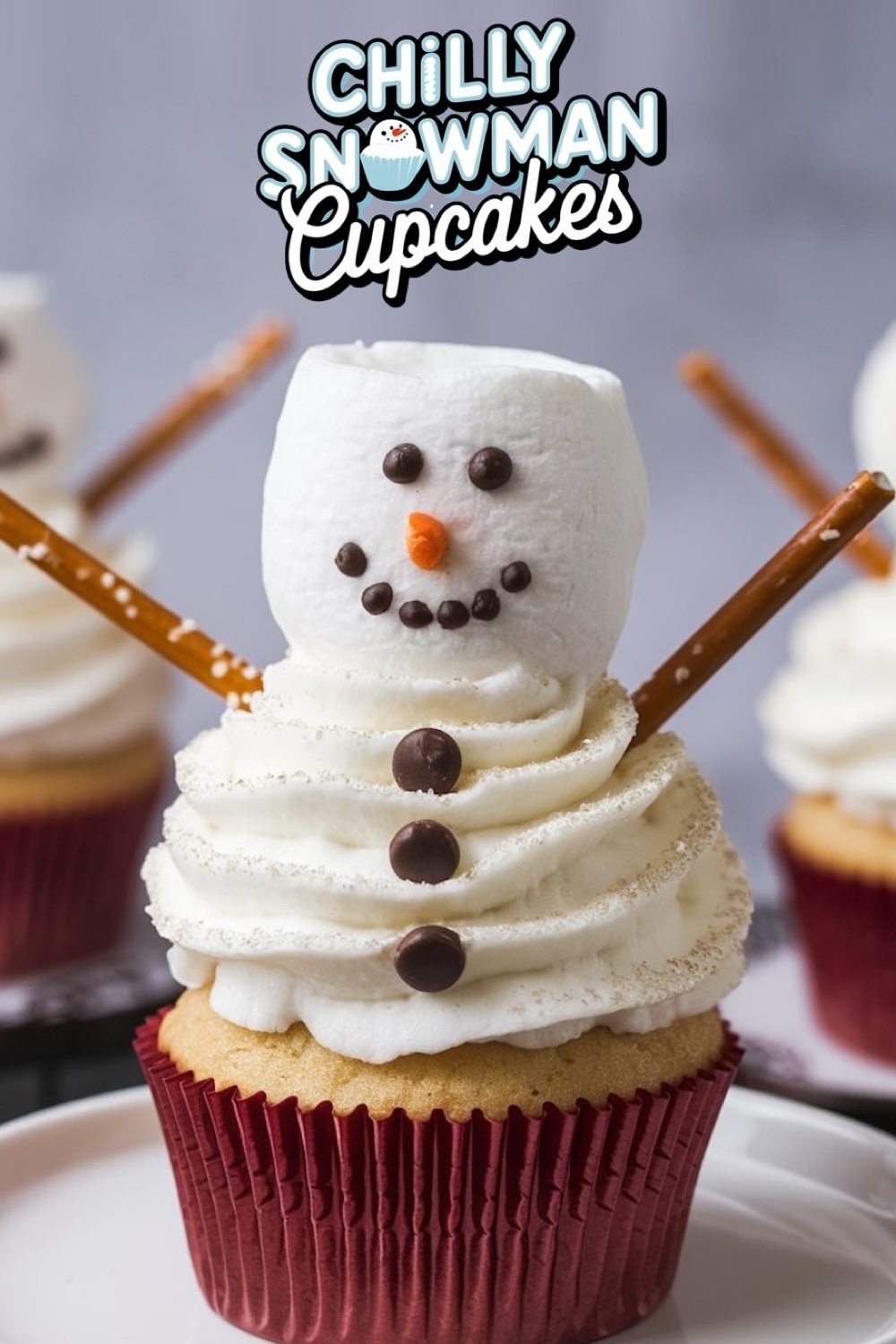 A pinterest format image for Chilly Snowman Cupcakes featuring a cupcake topped with a marshmallow snowman with a pretzel stick arms, chocolate chip buttons, and a carrot nose, against a blurred background.
