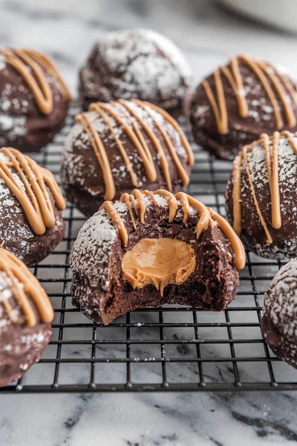 Chocolate snowballs with a peanut butter center, showcased on a cooling rack, each snowball adorned with a peanut butter drizzle and dusting of powdered sugar, capturing a cozy, holiday vibe.