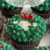 An array of chocolate wreath cupcakes, each topped with a creamy white circle center, green frosting, and red bow, set on a white plate.