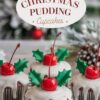 Festive Christmas pudding cupcakes, topped with a smooth white glaze that drips down the sides, adorned with a bright red cherry and green holly leaf decorations. The background features a cozy holiday scene with frosted decorations, enhancing the seasonal theme.