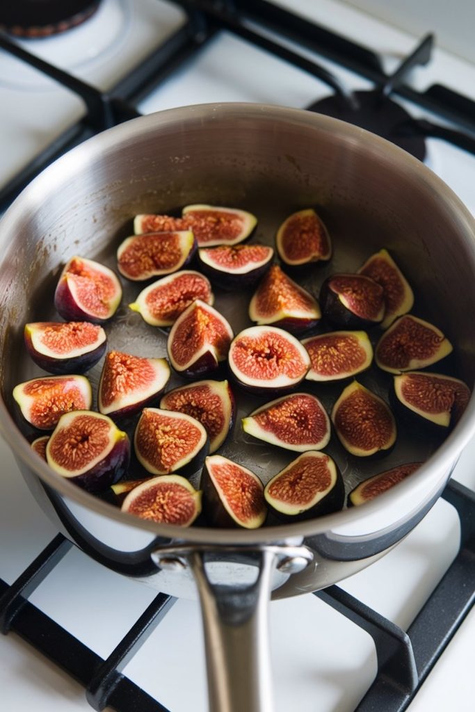 Halved fresh figs in a stainless steel pot, ready to be cooked on a gas stove, the beginning step of making fig jam
