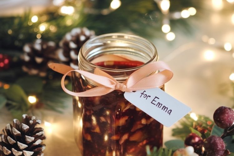 A mason jar filled with fig and walnut jam, tied with a pink ribbon and a tag labeled 'for Emma', placed among Christmas lights and pinecones for a festive presentation.