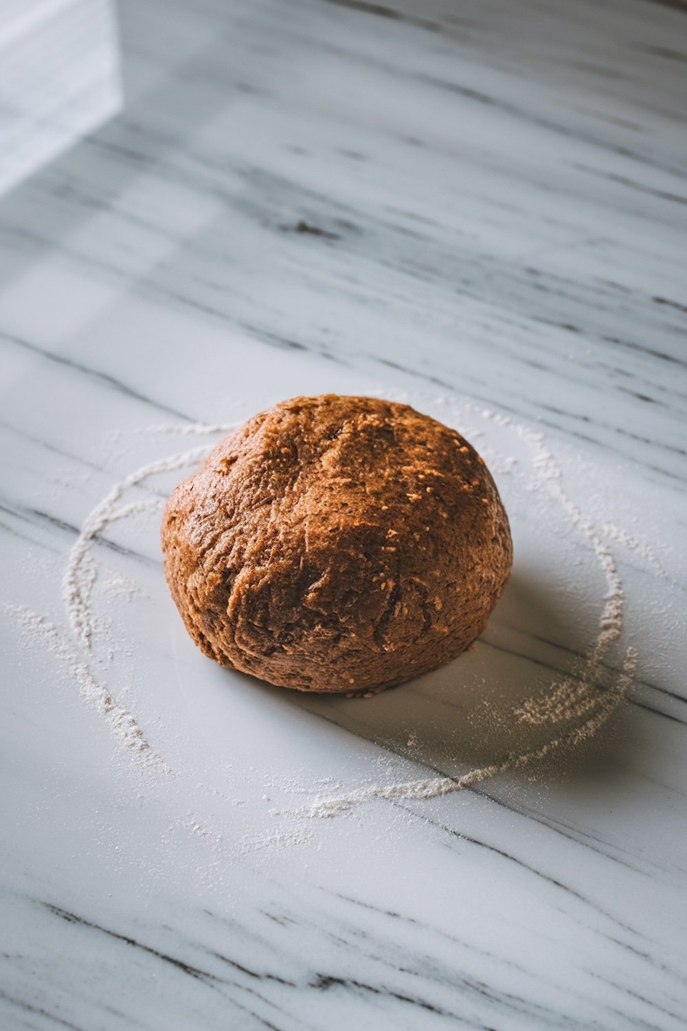 A smooth ball of gingerbread dough rests on a lightly floured marble countertop, ready for rolling and cutting. This step captures the early stages of baking holiday cookies, showing the rich, spiced dough ideal for creating gingerbread men.