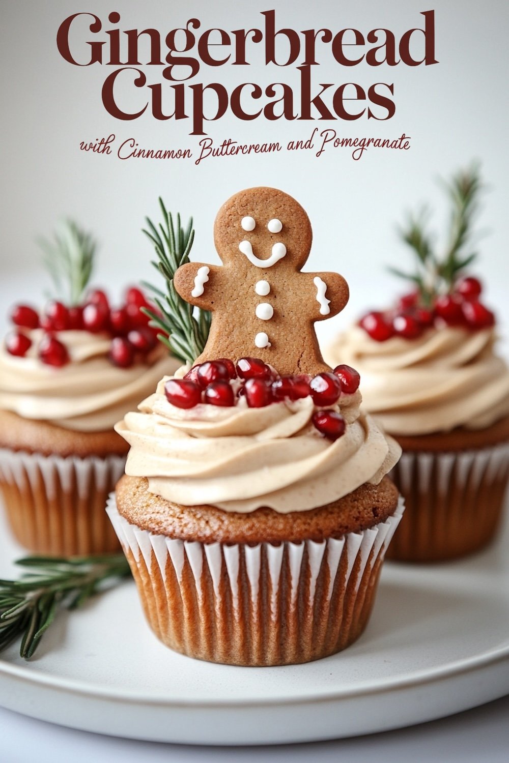 Close-up of a beautifully decorated gingerbread cupcake with cinnamon buttercream frosting. A smiling gingerbread man cookie sits atop a ring of juicy pomegranate arils, accented with rosemary sprigs, creating a festive and rustic holiday feel ideal for Christmas or winter-themed desserts.
