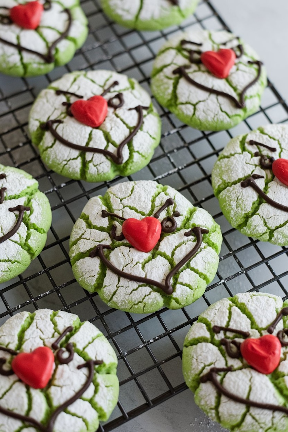 Green crinkle cookies inspired by the Grinch character, perfect for Christmas baking. Cracked, powdered sugar finish that reveals vibrant green underneath, with whimsical chocolate icing faces and bright red heart-shaped noses. Set on a cooling rack, these playful holiday treats are both eye-catching and delicious, ideal for holiday parties, Christmas cookie exchanges.