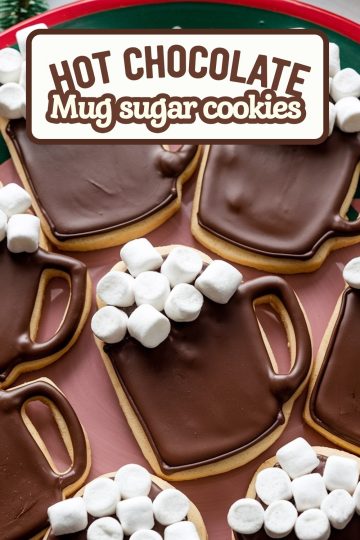 Festive "Hot Chocolate Mug" sugar cookies decorated with rich chocolate icing and topped with mini marshmallows to resemble a cozy cup of hot cocoa. These adorable cookies are perfect for winter gatherings or holiday baking, arranged on a red tray that enhances their seasonal charm.