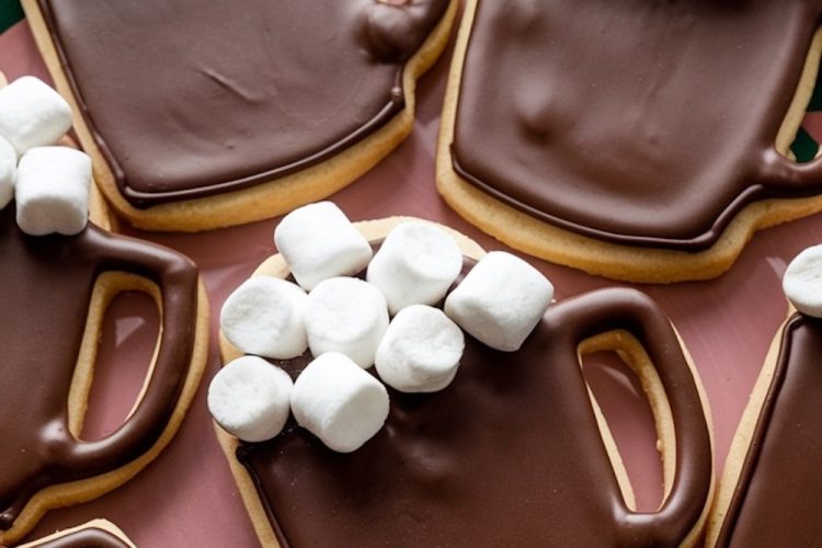 Festive "Hot Chocolate Mug" sugar cookies decorated with rich chocolate icing and topped with mini marshmallows to resemble a cozy cup of hot cocoa. These adorable cookies are perfect for winter gatherings or holiday baking, arranged on a red tray that enhances their seasonal charm.