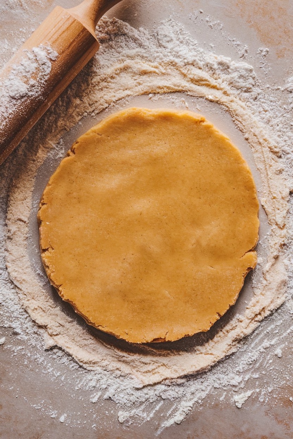 A smooth circle of sugar cookie dough on a floured surface, ready for rolling and cutting into shapes. This dough preparation shot showcases the early stage of creating holiday-themed cookies, perfect for adding a personal touch to Christmas desserts.
