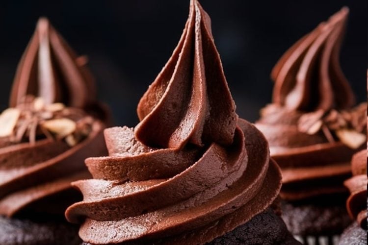 A selection of moist chocolate cupcakes, all frosted with tall, elegant swirls of chocolate buttercream, standing on a dark, rustic surface. The frosting has a smooth and luscious texture, while the cupcakes themselves are dark and rich. A sprinkle of chocolate shavings can be seen on a few of the cupcakes, adding extra detail and decadence.