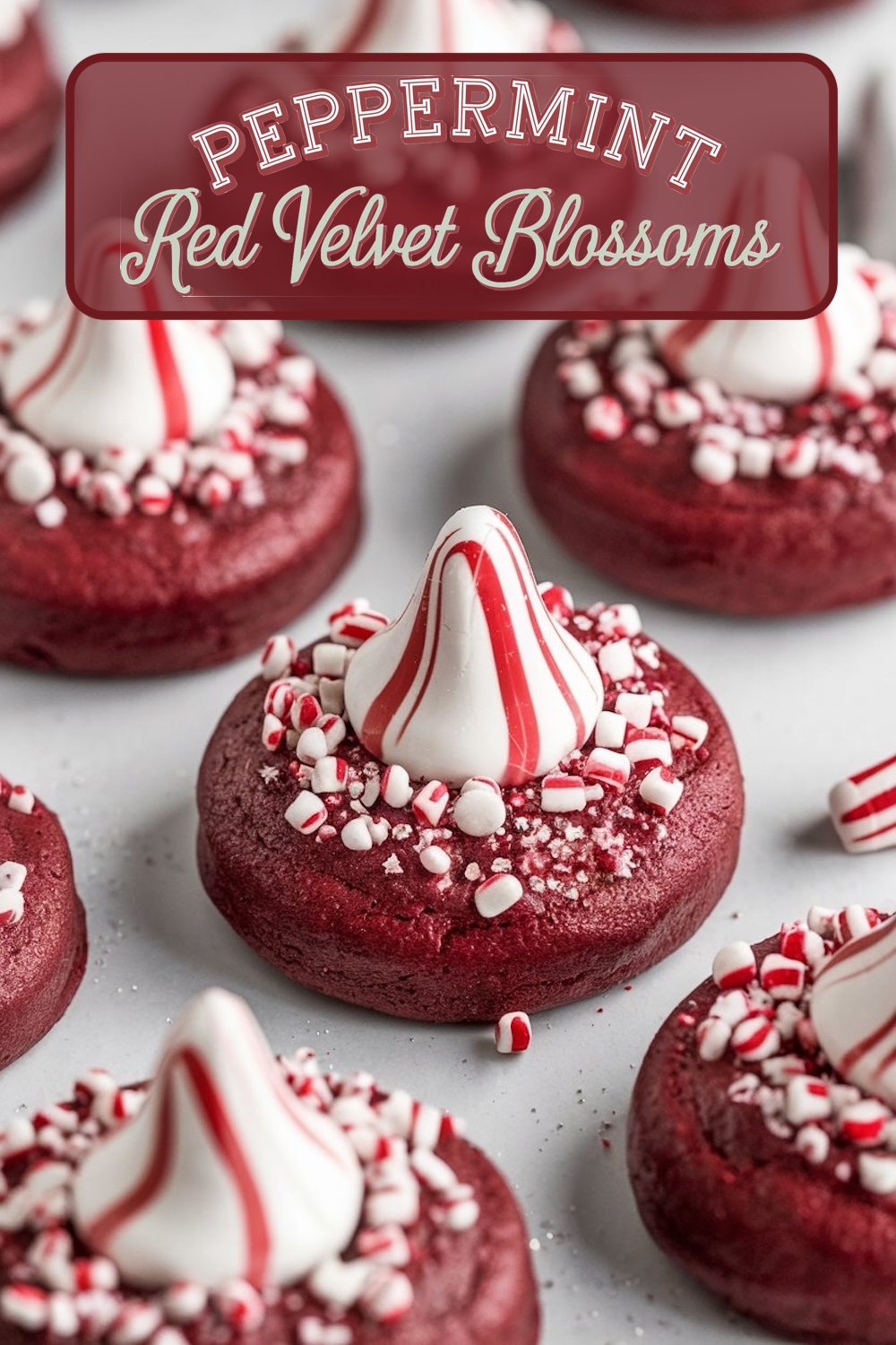 Red velvet peppermint blossom cookies neatly lined up, each topped with a peppermint swirl kiss and surrounded by crushed candy canes. The cookies’ rich red hue combined with the white peppermint candy offers a visually appealing treat ideal for holiday cookie exchanges or Pinterest boards.