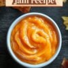 Top view of a bowl of smooth pumpkin jam on a dark wooden surface, surrounded by autumn leaves, with 'Pumpkin Jam Recipe' text overlay.