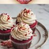 Three red velvet cupcakes topped with swirls of cream cheese frosting and red crumbs on an elegant plate.