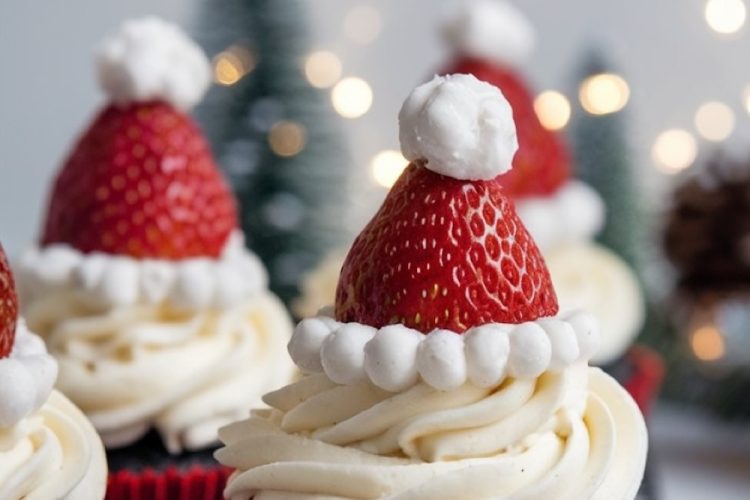 Festive Santa hat cupcakes topped with fresh strawberries and whipped cream resembling Santa's hat. The cupcakes have a rich chocolate base and are decorated with red liners, perfect for Christmas celebrations.