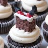 Christmas cupcake featuring a playful "Santa Stuck in the Chimney" design. A chocolate cupcake with smooth white buttercream frosting is topped with a fondant decoration resembling Santa's legs and black boots sticking out of a brick chimney, adding holiday cheer and whimsical charm to any dessert table