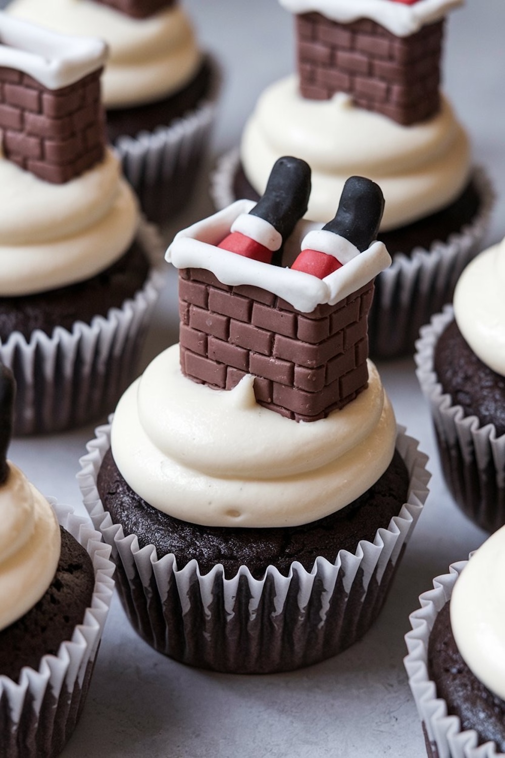 Close-up of "Santa Stuck in the Chimney" cupcakes with detailed fondant work. The decorations show Santa's boots and red pants poking out from a fondant brick chimney, resting on thick swirls of frosting, capturing the magic of Christmas in a fun and edible way.