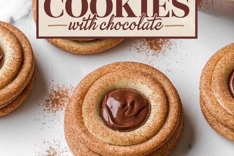 A close-up view of snickerdoodle thumbprint cookies filled with glossy chocolate on a marble surface, dusted with cinnamon.