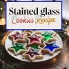Holiday-themed image of "Stained Glass Cookies" on a decorative plate, styled with festive elements. The star-shaped sugar cookies feature vibrant translucent centers in red, green, and blue, creating a stained-glass effect that catches the warm glow of nearby lights. Perfect for Christmas baking inspiration or holiday dessert tables.