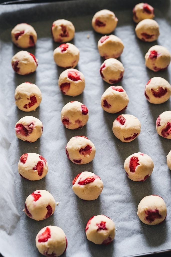 Unbaked balls of strawberry shortbread cookie dough on parchment paper, each with a visible chunk of strawberry.