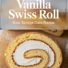 Close-up of a sliced vanilla Swiss roll sponge cake on parchment paper, highlighting a golden sponge texture wrapped around a thick layer of creamy whipped filling, with powdered sugar sprinkled on the surface.