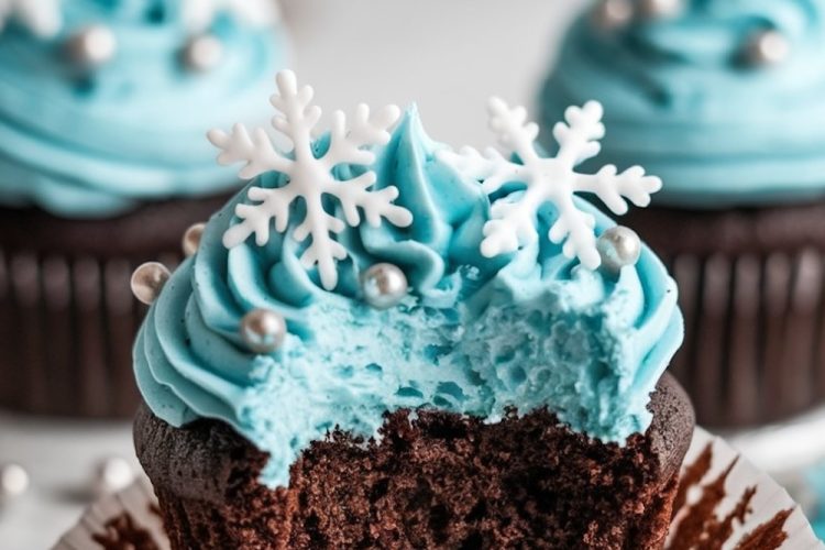 A single chocolate cupcake with vibrant blue frosting topped with a white fondant snowflake and silver edible pearls, presented on a dark background with a 'Winter Wonderland Chocolate Cupcakes' banner above.