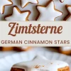 Iced cinnamon star cookies arranged on a white surface, each cookie topped with a smooth white glaze, with one partially eaten cookie showing a spiced almond interior.