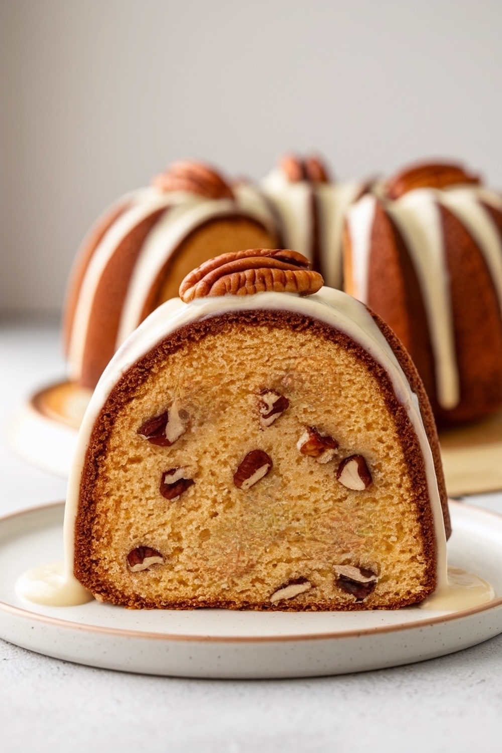 A beautifully baked butter pecan pound cake displayed on a plate, with its rich, moist crumb and pecan-filled interior visible. Topped with a thick glaze and a pecan garnish, the dessert is styled as an elegant centerpiece on a neutral background.
