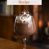 A glass of chocolate mousse garnished with whipped cream and chocolate shavings, styled on a wooden table with a cozy, warmly lit background. The text overlay reads "Chocolate Mousse Recipe" in bold, elegant typography, emphasizing the dessert's decadent and indulgent appeal.