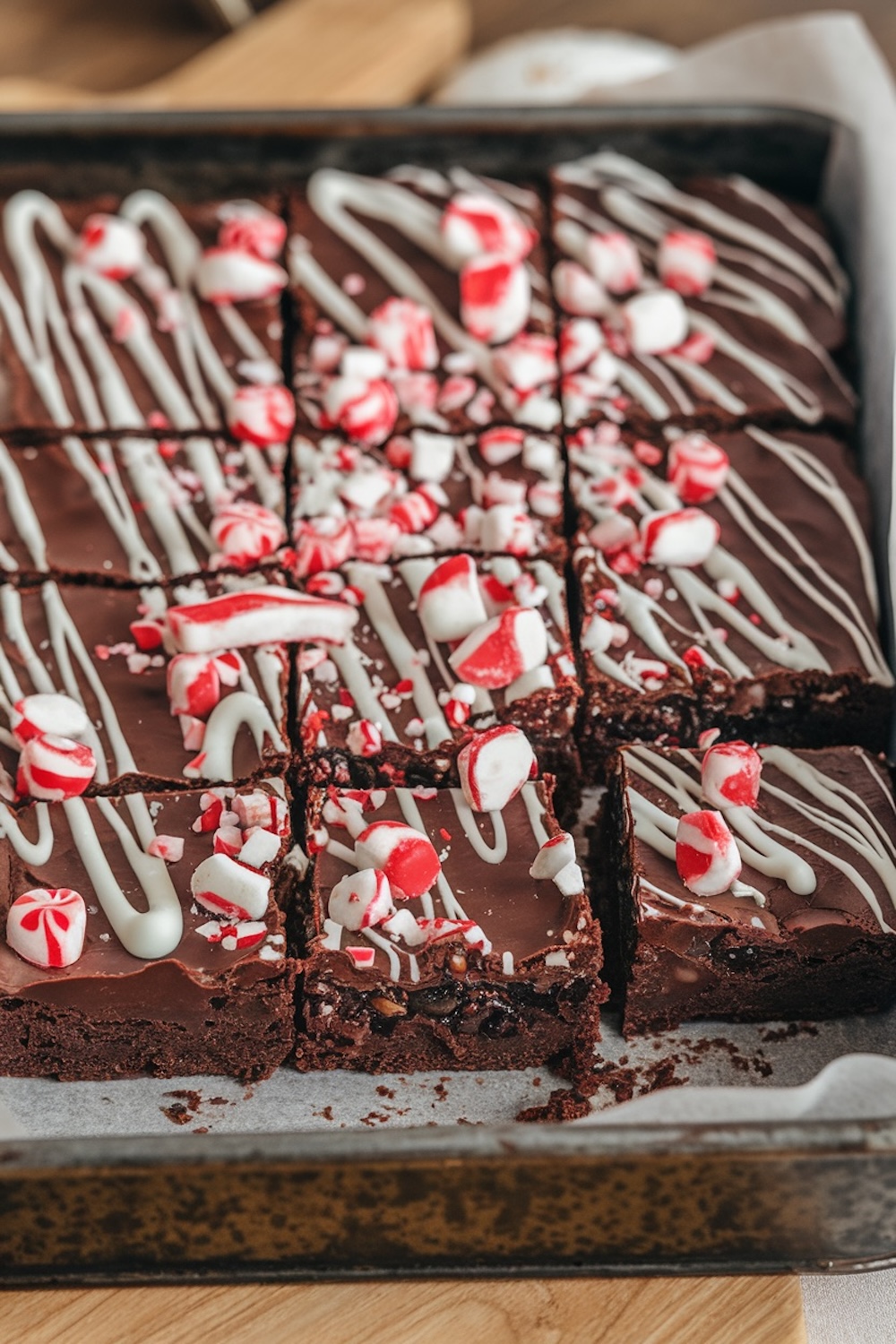 A baking pan filled with freshly baked chocolate peppermint brownies, decorated with white chocolate drizzle and crushed peppermint candy. The vibrant red and white candies add a festive touch, making these brownies visually appealing and ideal for Christmas treats.