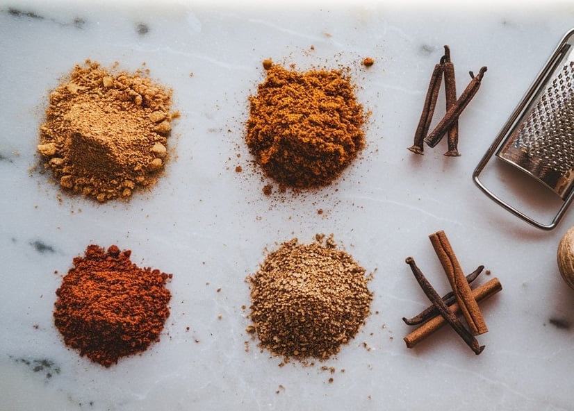 A layout of aromatic holiday spices, including ground ginger, cinnamon, nutmeg, and cloves on a marble surface, emphasizing the flavors used in gingerbread recipes.