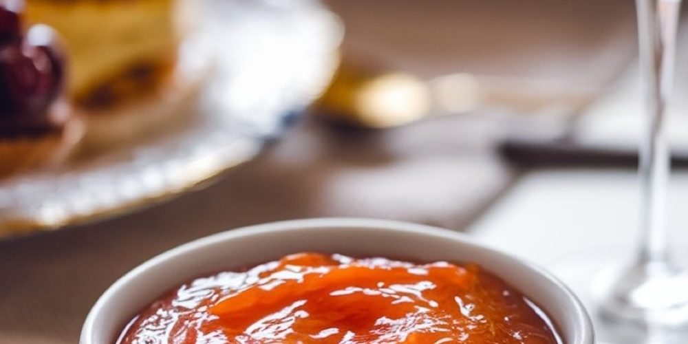A beautifully styled breakfast scene featuring a bowl of orange jam on a table with pastries, fresh fruit, and a glass of orange juice. This orange jam is ideal for elevating any morning spread with a zesty, homemade touch.