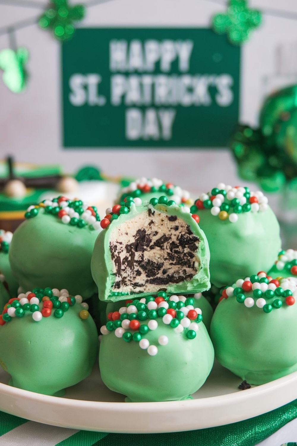 St. Patrick's Day-themed display of Irish Cream Oreo truffles on a white plate. A backdrop with "Happy St. Patrick's Day" enhances the festive mood, while the sprinkles and green candy coating make these truffles a visually enticing addition to holiday celebrations.